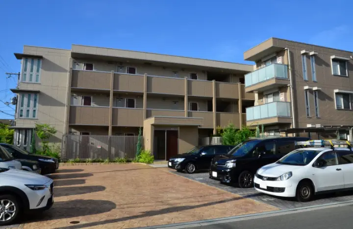 青空の下に建つ3階建ての現代的なアパートの外観が映されている