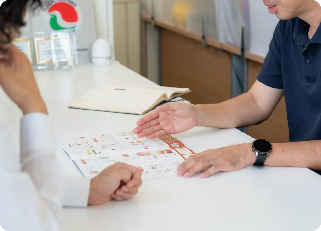 2人の男性がテーブル越しにパンフレットを見ながら説明や相談をしている様子